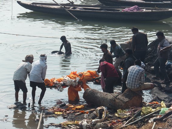A body being  bathed in the Ganges while someone pans for gold in the background